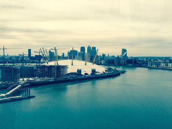 View of city at waterfront against cloudy sky