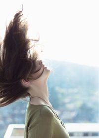 Young woman tossing hair against sky