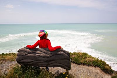 Rear view of woman sitting on bench against sea