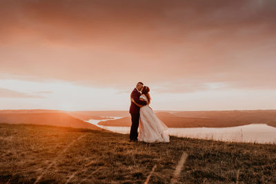 Rear view of woman standing on field against sky during sunset