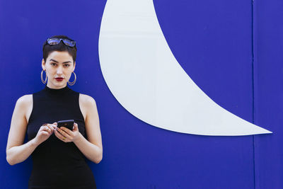 Smiling woman using phone while standing against blue background