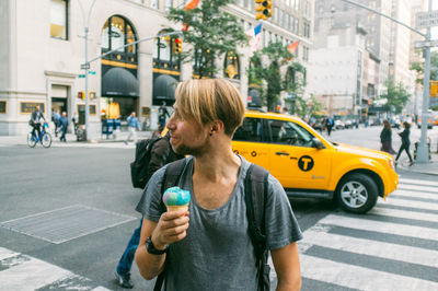 Smiling young man holding ice cream while looking away in city