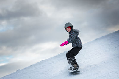 Full length of girl snowboarding on snow covered mountain against sky