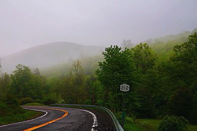 Road amidst trees against mountains during foggy weather