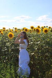 Woman standing on yellow flowering plants on field against sky