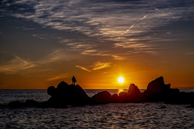 Silhouette rocks on sea against sky during sunset