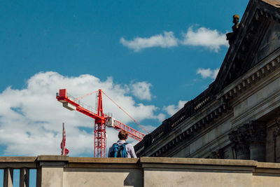 Rear view of man standing by historic building against crane