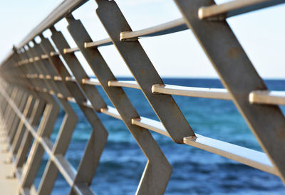 Close-up of metallic railing at beach against sky