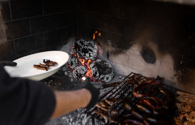 Unrecognizable man picking up the meat from a firewood barbecue with coals in the background.