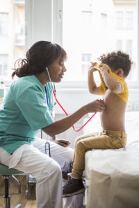 Female pediatrician listening to boy's heartbeat in medical clinic