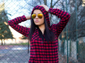 Young woman wearing sunglasses standing against fence