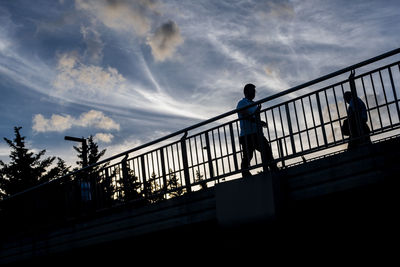 Silhouette man standing on footbridge against sky