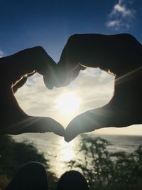 Person hand holding heart shape against sky