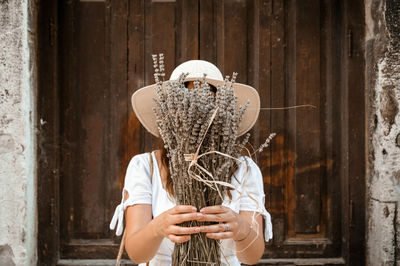 Front view of young woman holding dried lavender bundle in front of her face.
