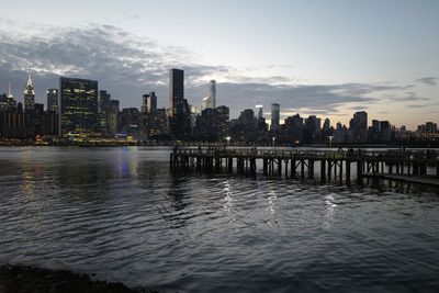 Pier on lake against illuminated buildings at gantry plaza state park