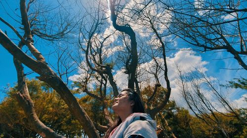Low angle view of woman looking at bare tree against sky