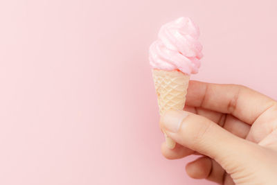 Hand holding ice cream cone against pink background