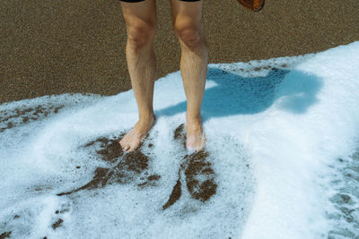 Low section of man standing on a wave foam