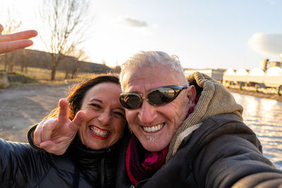 Middle aged couple wearing winter clothes taking a selfie on the river banks - people in recreation