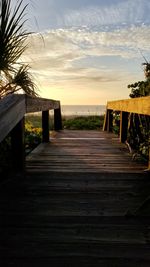 Wooden railing by footpath against sky during sunset