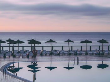 Beach umbrellas reflecting in the pool against sky at sunrise with beautiful colors