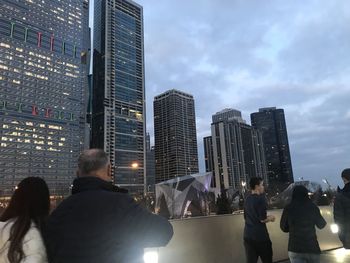 People on modern buildings in city against sky