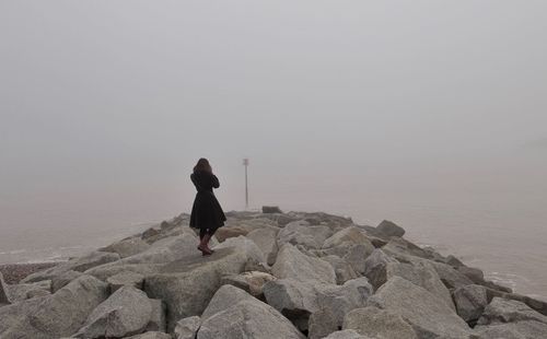 Rear view of woman standing on beach against clear sky