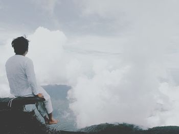 Full length of man sitting on cliff against sky