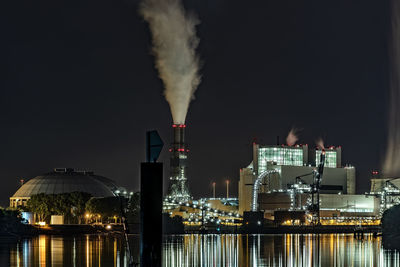 Smoke emitting from illuminated factory against sky at night