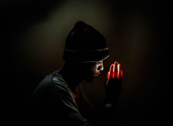 Close-up of man with illuminated hands clasped against black background