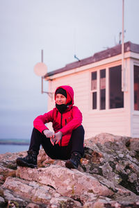 Smiling woman sitting on rock against cabin