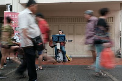 Man playing guitar while people walking in city