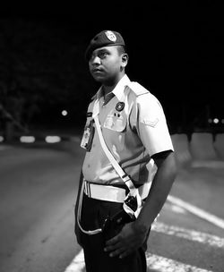 Police man looking away while standing on road at night