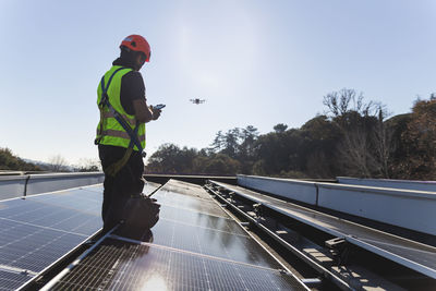 Mature engineer flying drone standing by solar panel