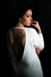 Rear view of woman wearing sweater with tattoo on back against black background