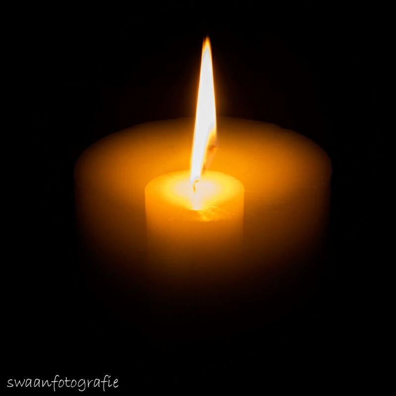 CLOSE-UP OF LIT CANDLES IN DARK ROOM