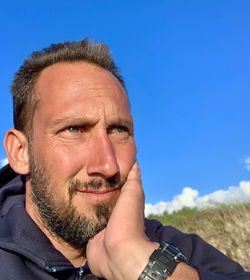 Close-up of thoughtful mature man against blue sky