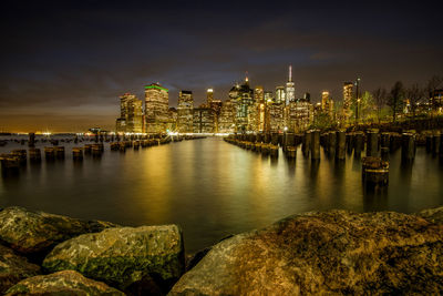 Illuminated buildings by river against sky at night