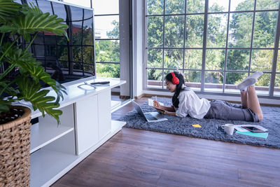 Side view of man sitting on window at home