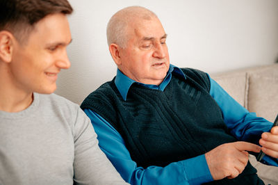 Man with grandfather using smart phone at home