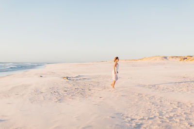 Side view of young woman walking at beach against clear sky during sunset