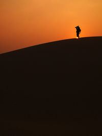 Silhouette man standing on land against sky during sunset