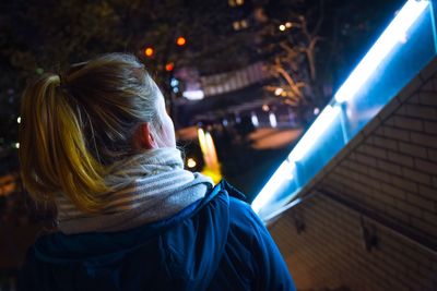 Rear view of woman with ponytail walking by illuminated wall at night