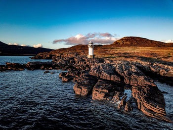 Lighthouse on rock by sea against blue sky