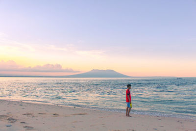 Man standing on beach against sky during sunset