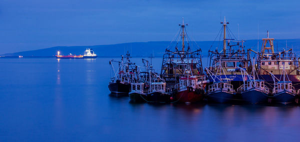 Boats moored at harbor against sky at dusk