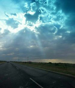 Road passing through field against cloudy sky