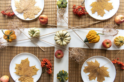 Flat lay of small pumpkins and dry brown maple leafs on white plates, autumn dinner table decors