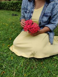 Midsection of woman holding red flower on field