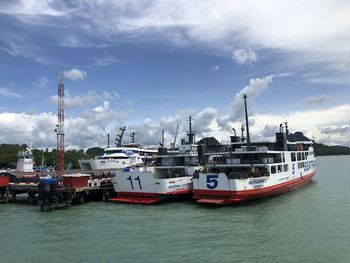 Fishing boats moored at harbor against sky